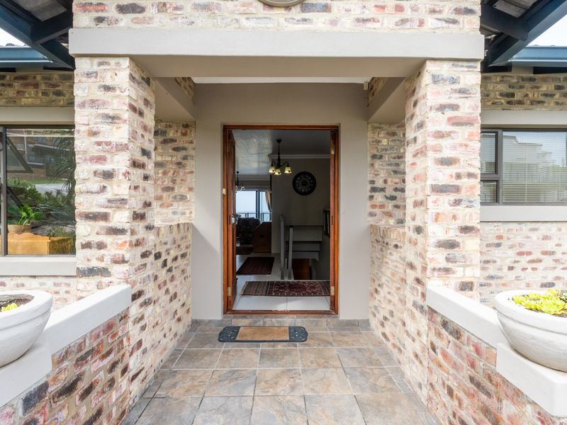 A welcoming front entrance featuring a face brick facade, tiled porch area, and timber-framed doorway leading into the home.