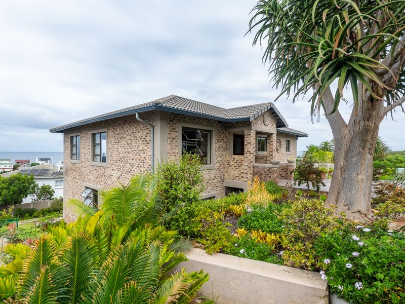 A well-maintained face brick house featuring a tiled roof, casement windows, and established garden landscaping, situated in a coastal residential area.