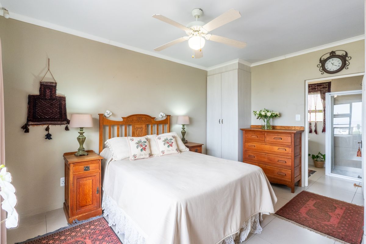 A well-maintained bedroom featuring neutral wall tones, tiled flooring, a ceiling fan, and a built-in wardrobe with direct access to an en-suite bathroom.