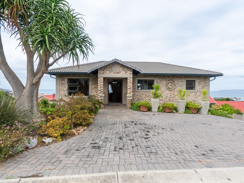 A well-maintained single-story brick home featuring a paved driveway, covered entrance, and established garden landscaping.