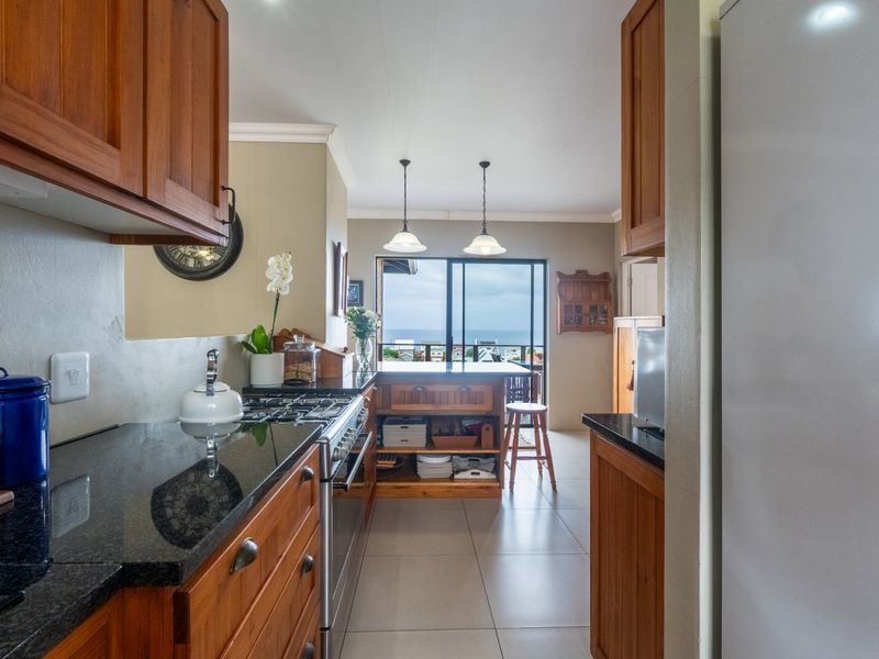Open plan kitchen featuring wooden cabinetry, granite countertops, and a gas hob, flowing into a dining area with sliding doors and ocean views.