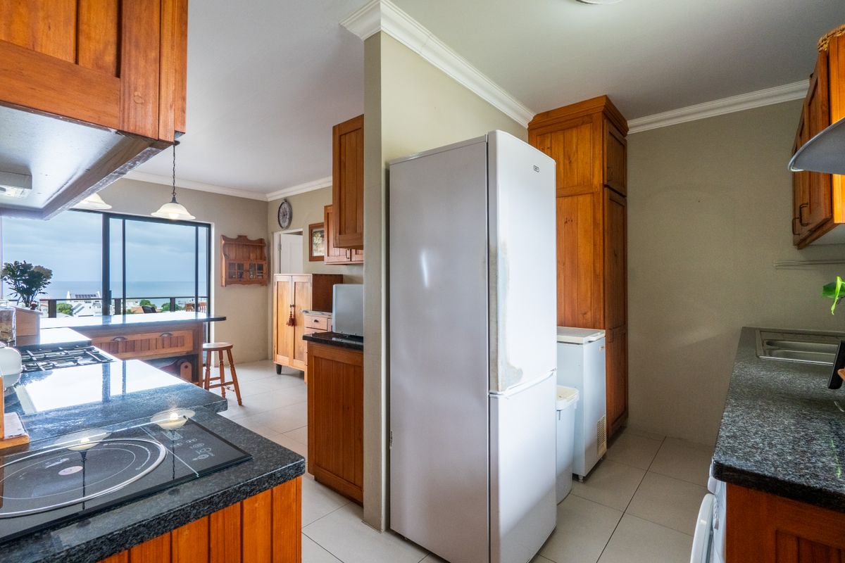 A functional kitchen featuring wooden cabinetry, granite countertops, and built-in appliances, with an open-plan layout leading to a dining area with ocean views.