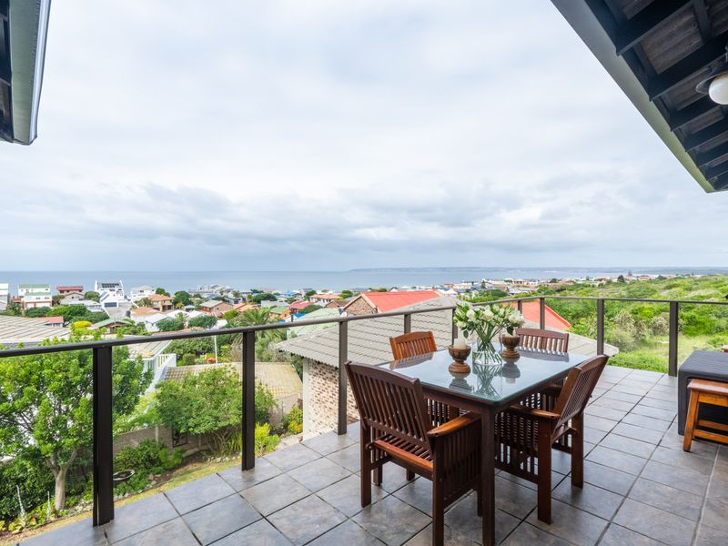 A covered balcony featuring tiled flooring and a metal balustrade, offering expansive coastal and neighborhood views.