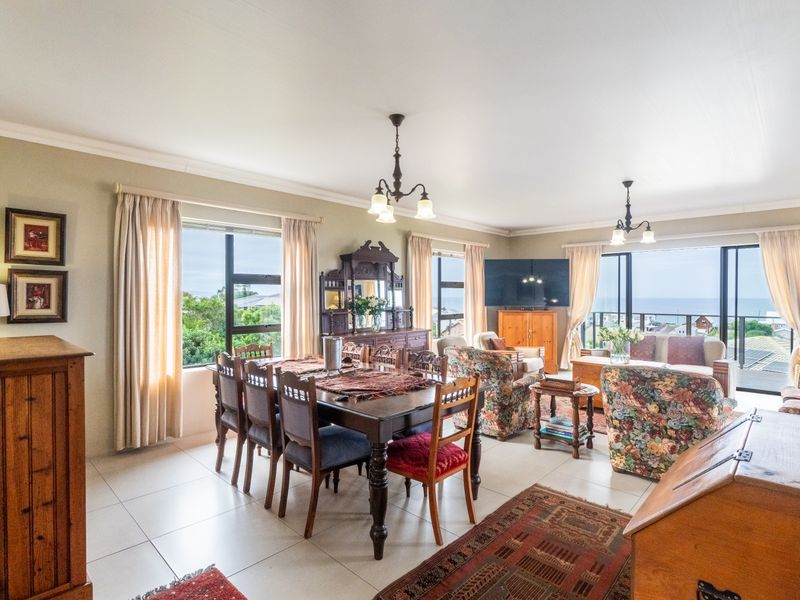 Spacious open-plan living and dining area featuring tiled floors, large windows, and sliding glass doors leading to an outdoor balcony with coastal views.