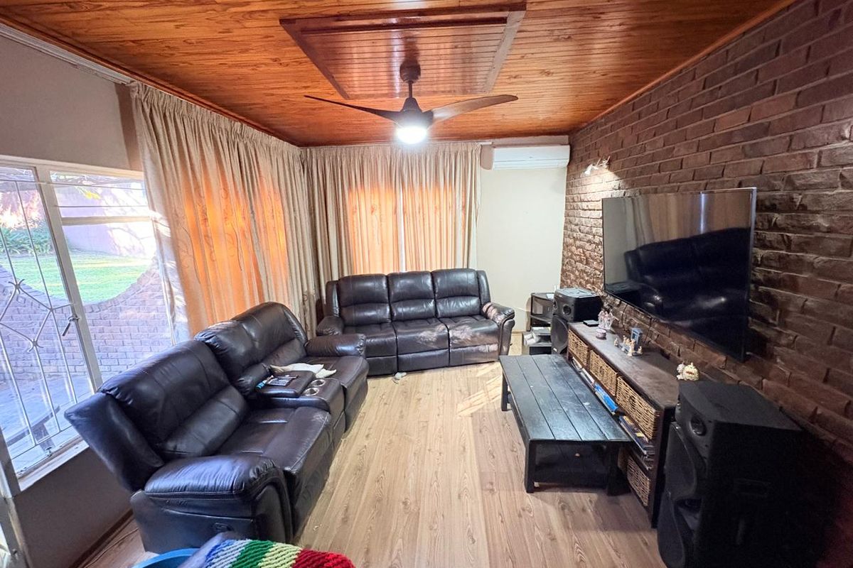 Cozy living room featuring a warm timber ceiling, exposed brick feature wall, laminate flooring, and a split-system air conditioner for climate control.