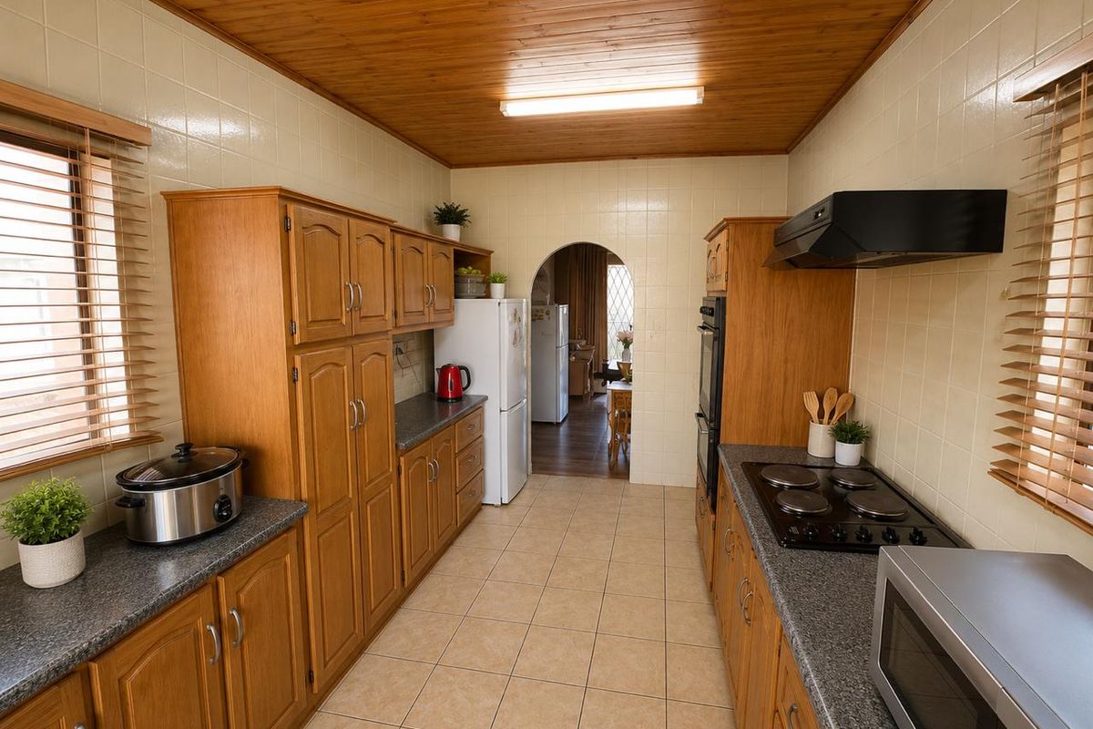 A functional kitchen featuring wooden cabinetry, tiled surfaces, and built-in appliances, with a classic design and direct access to the adjacent living area.
