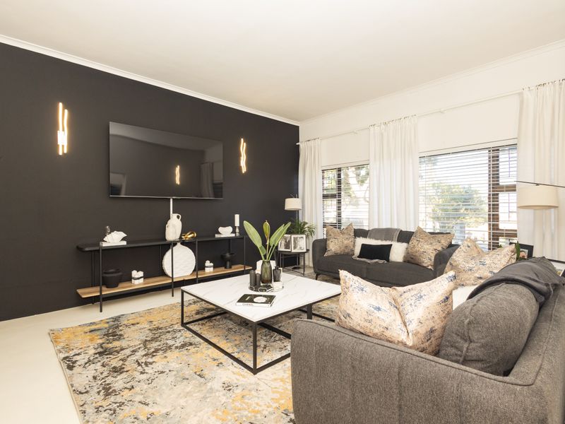 A modern living room featuring a bold black accent wall, large windows with venetian blinds, and contemporary wall-mounted lighting fixtures.