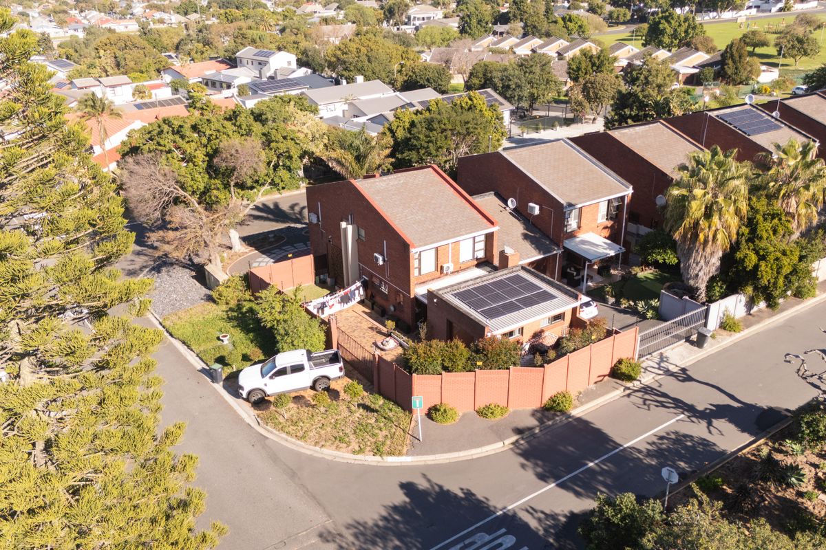 Aerial view of a residential property featuring a brick exterior, tiled roof, solar panel installation, and a paved driveway within a suburban neighborhood.