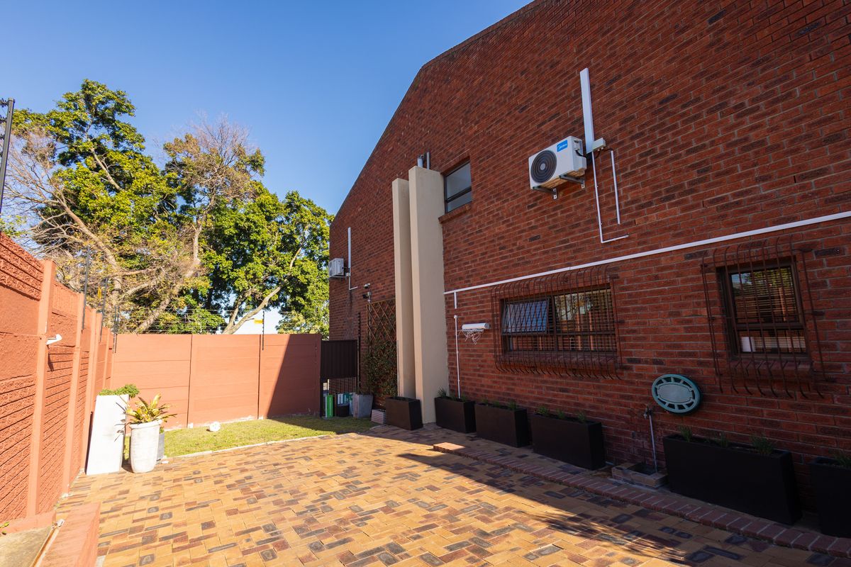 Rear exterior view featuring a brick facade, paved patio area, security bars on windows, and perimeter boundary wall with electric fencing.