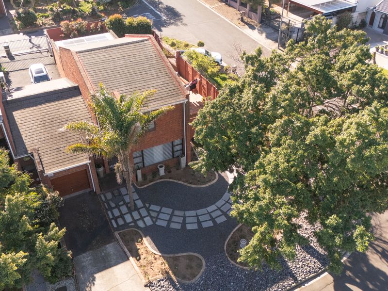 Aerial view of a residential property featuring a brick facade, tiled roof, paved driveway, and a well-maintained landscaped front garden.