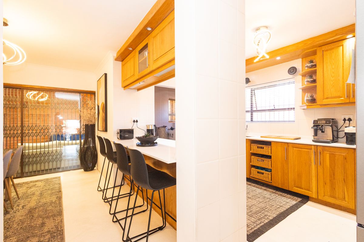 A functional kitchen featuring warm wooden cabinetry, a breakfast bar, and tiled finishes, offering a practical layout with good natural light.