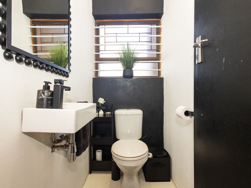 Compact guest bathroom featuring a wall-mounted basin, toilet, and security bars on the window, finished with a modern black and white color scheme.