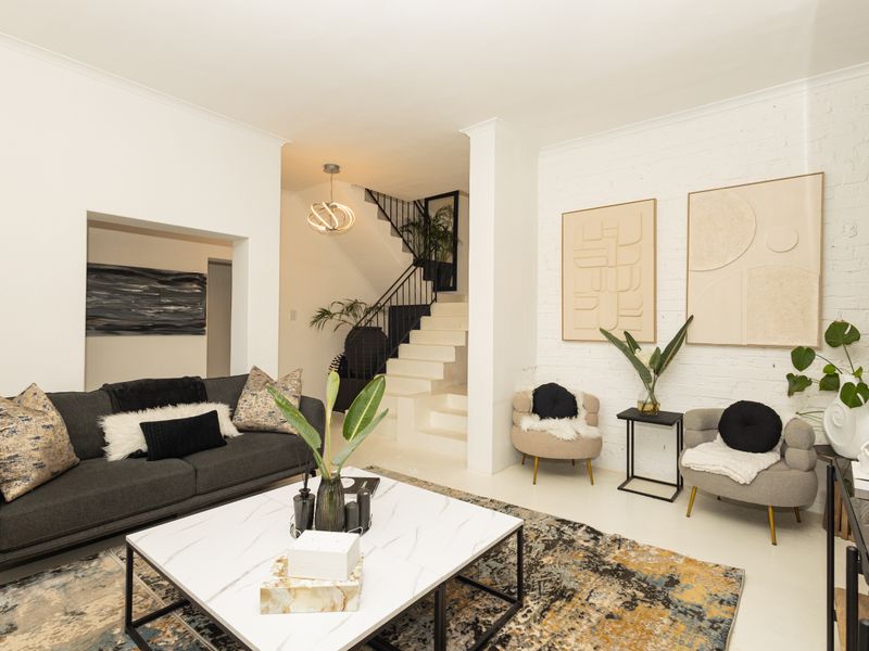 A bright and modern living room featuring an exposed brick wall, a staircase with a decorative wrought iron balustrade, and a recessed wall niche.