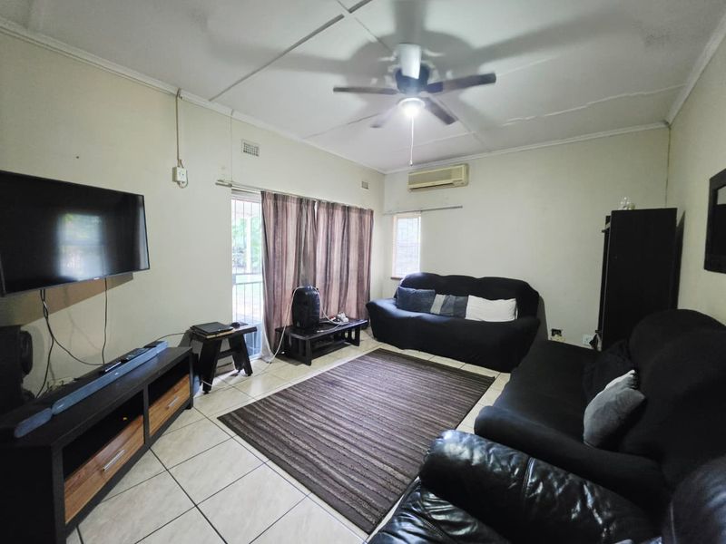 A living room featuring tiled flooring, a ceiling fan, and a wall-mounted air conditioning unit with access to an outdoor area via a sliding door.