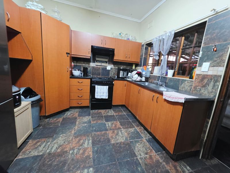 A functional kitchen featuring wood-look laminate cabinetry, dark tiled flooring, a built-in oven with extractor fan, and a stainless steel sink.