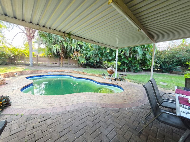 Outdoor entertainment area featuring a covered patio with brick paving overlooking a swimming pool and established garden.