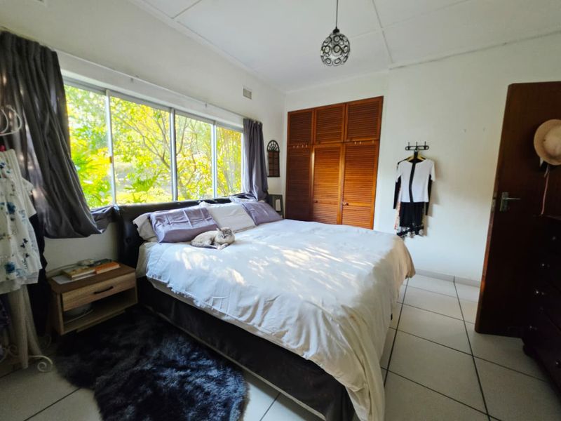 A bright bedroom featuring large sliding windows, tiled flooring, and built-in wooden wardrobe storage.