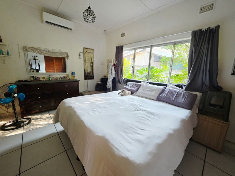 A functional bedroom featuring tiled flooring, a split-system air conditioner, and large windows providing natural light.