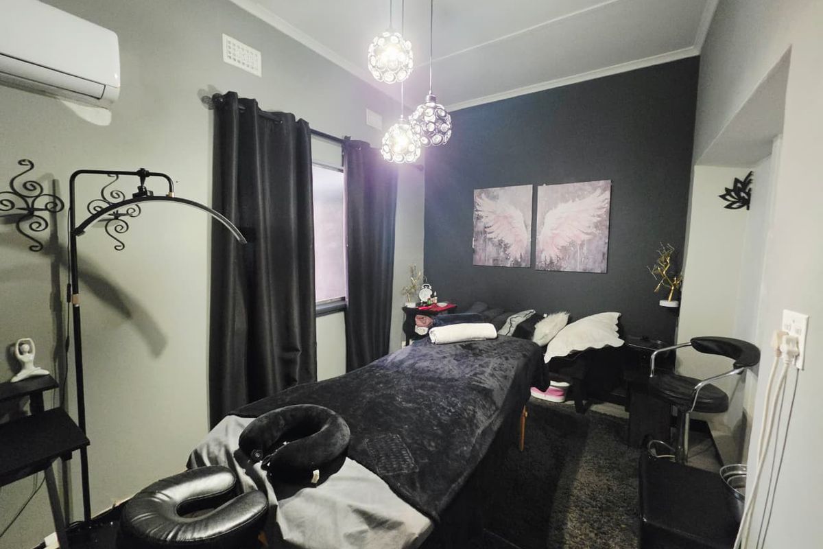 A bedroom currently utilized as a treatment room, featuring a split-system air conditioner, decorative pendant lighting, and a dark accent wall.