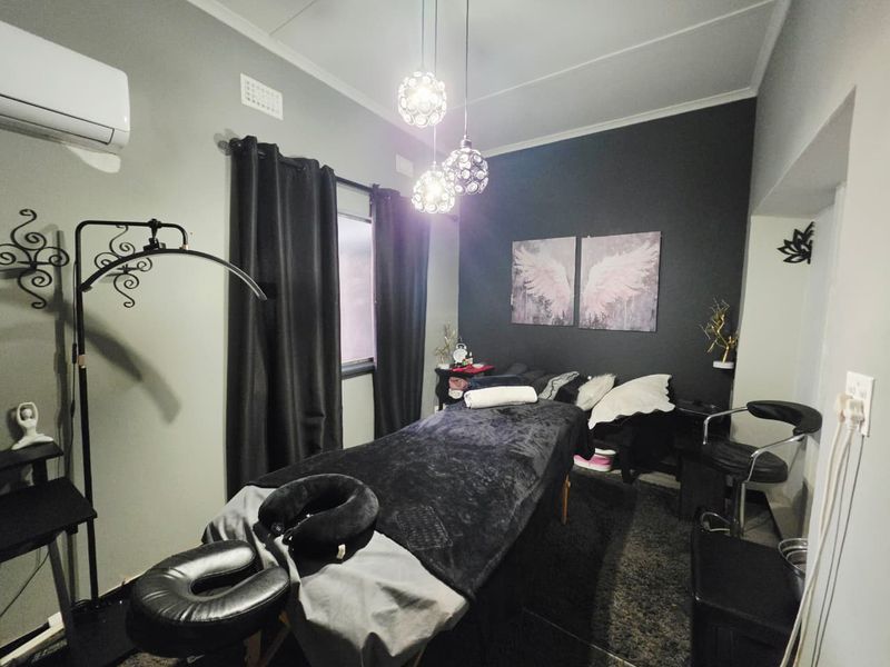 A bedroom currently utilized as a treatment room, featuring a split-system air conditioner, decorative pendant lighting, and a dark accent wall.