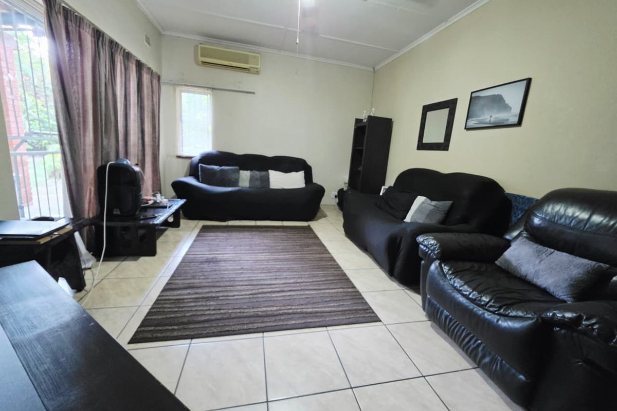 A functional living room featuring tiled flooring, a ceiling fan, and a wall-mounted split-system air conditioner.