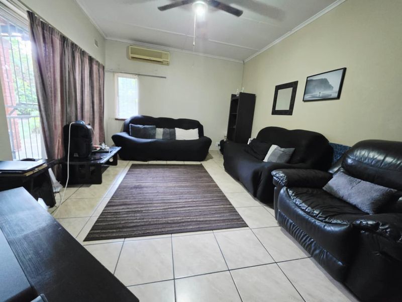 A functional living room featuring tiled flooring, a ceiling fan, and a wall-mounted split-system air conditioner.