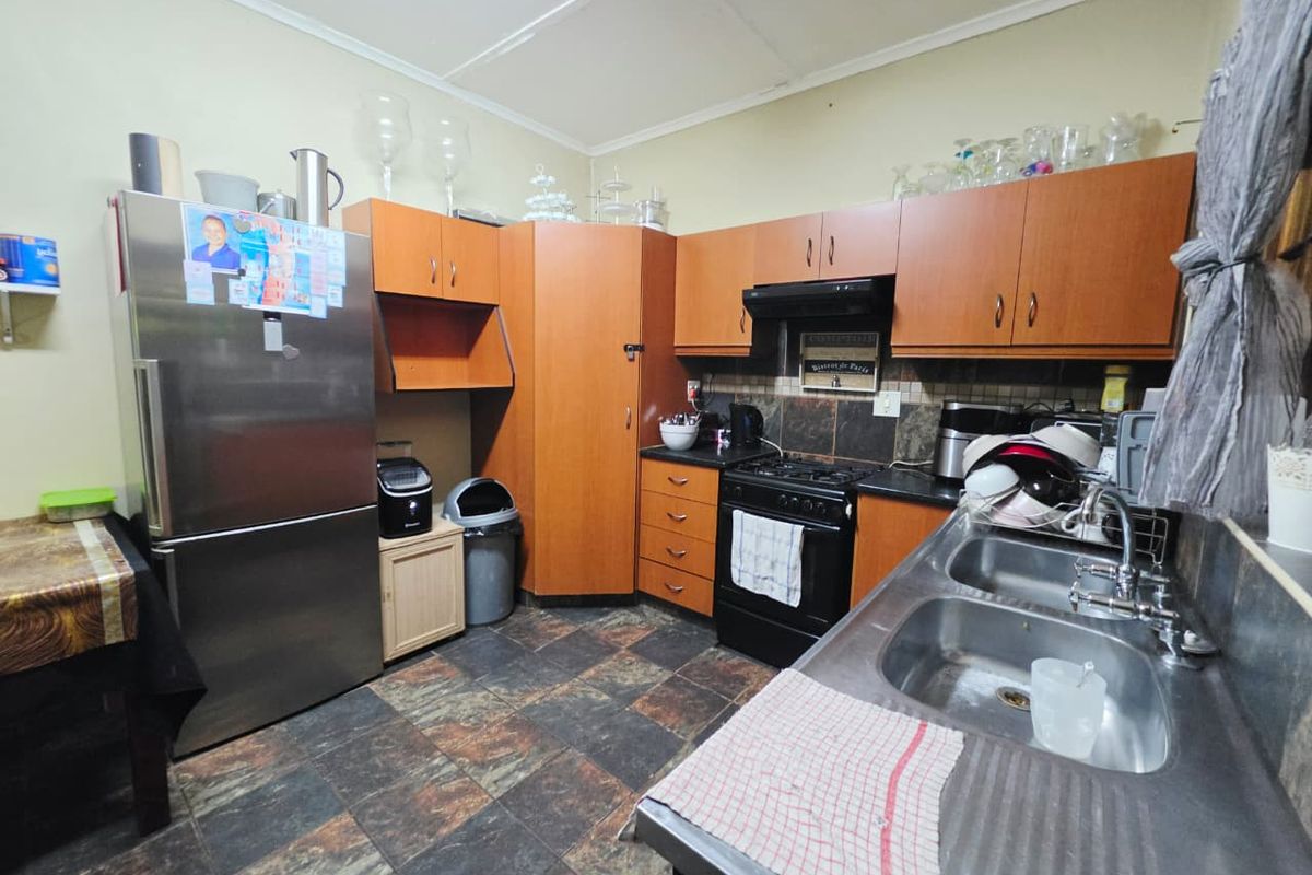 A functional kitchen featuring laminate cabinetry, a double bowl stainless steel sink, gas stove with extractor fan, and tiled flooring.