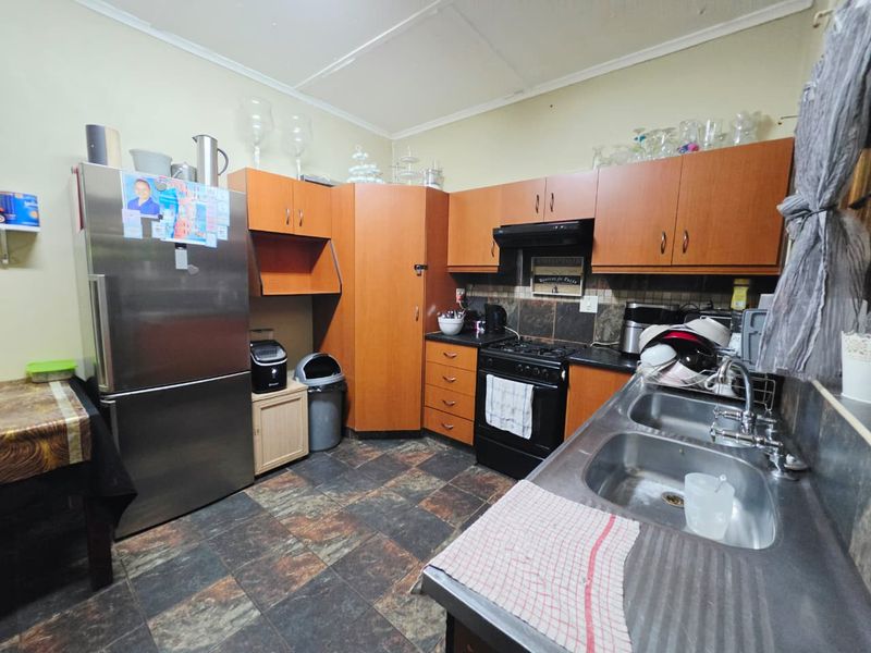 A functional kitchen featuring laminate cabinetry, a double bowl stainless steel sink, gas stove with extractor fan, and tiled flooring.