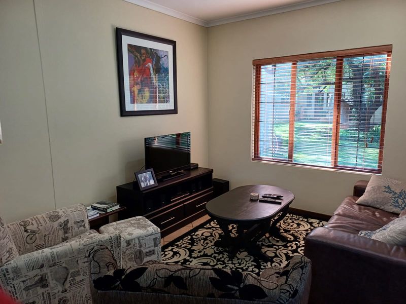 A comfortable living room featuring tiled flooring, wooden window frames with venetian blinds, and a view of the garden.