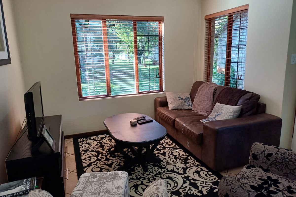 A comfortable living room featuring tiled flooring and large windows with wooden frames and venetian blinds, providing natural light and garden views.