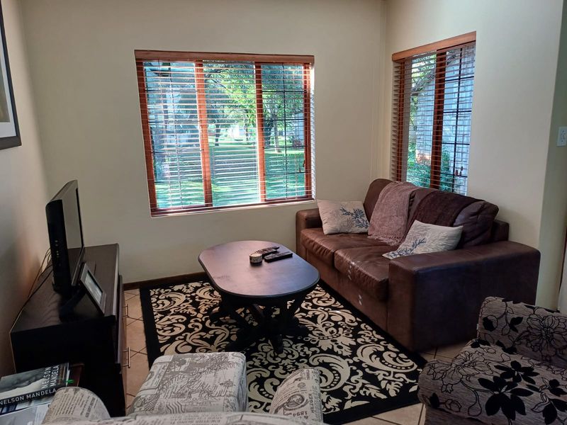 A comfortable living room featuring tiled flooring and large windows with wooden frames and venetian blinds, providing natural light and garden views.