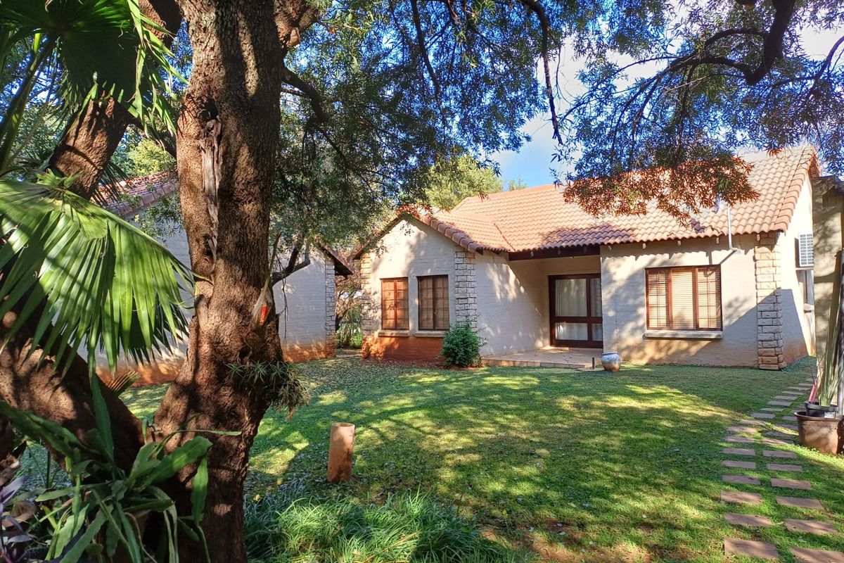 A view of the rear exterior of the townhouse, featuring a well-maintained garden, stone-clad accents, and a covered patio area.