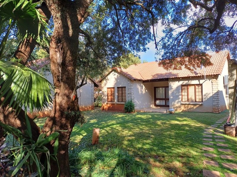 A view of the rear exterior of the townhouse, featuring a well-maintained garden, stone-clad accents, and a covered patio area.