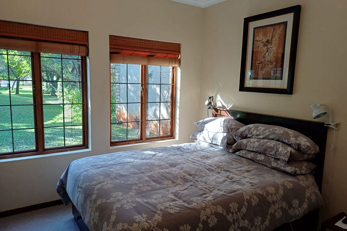 A cozy bedroom featuring timber-framed windows with bamboo blinds, offering natural light and views of the garden.