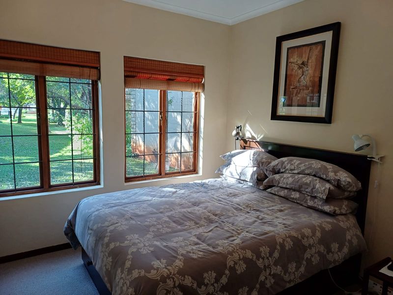 A cozy bedroom featuring timber-framed windows with bamboo blinds, offering natural light and views of the garden.