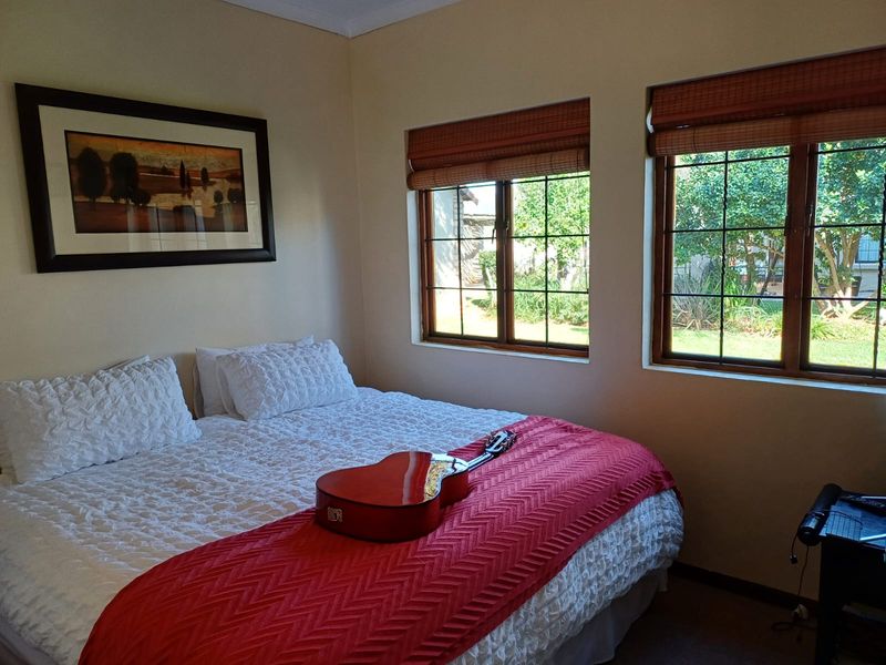 A cozy bedroom featuring timber-framed windows with bamboo blinds, offering natural light and views of the garden.