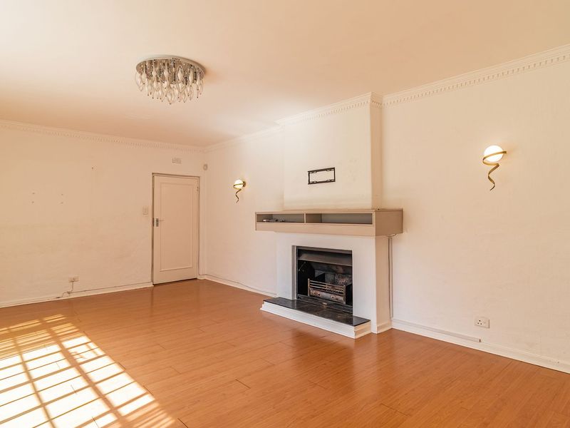 A spacious, empty living room featuring laminate flooring, a central fireplace, and decorative crown molding, ready for personalization.