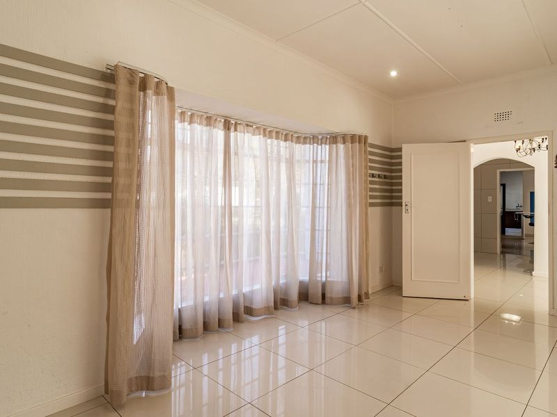 A bright and spacious living area featuring polished tiled flooring, a large bay window, and an open archway leading to adjacent rooms.