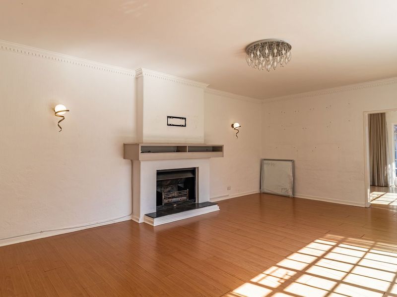 Spacious living room featuring laminate flooring, a central fireplace, crown molding, and access to an outdoor area through classic french doors.