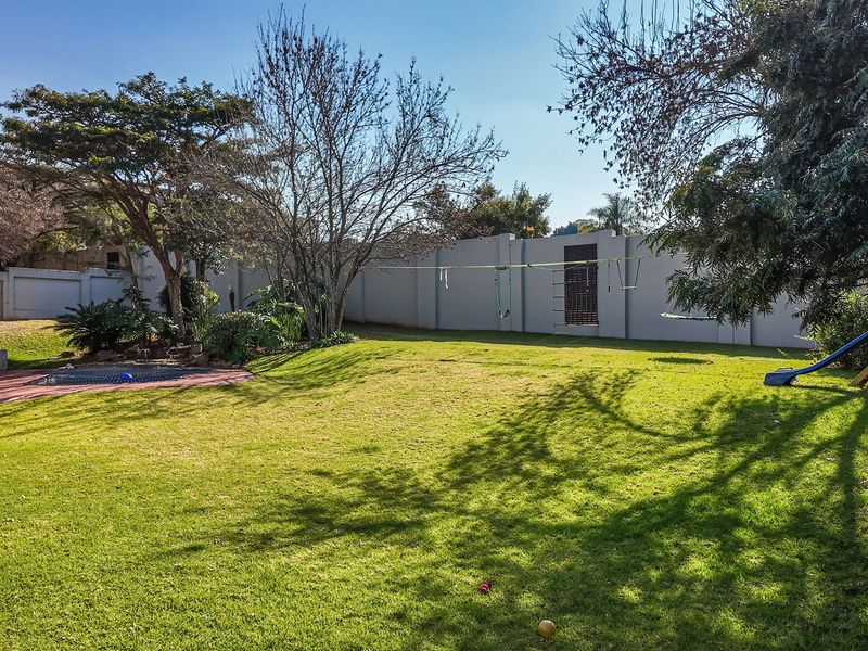 A spacious, well-maintained private garden featuring a lush lawn, mature trees, and a secure perimeter wall.
