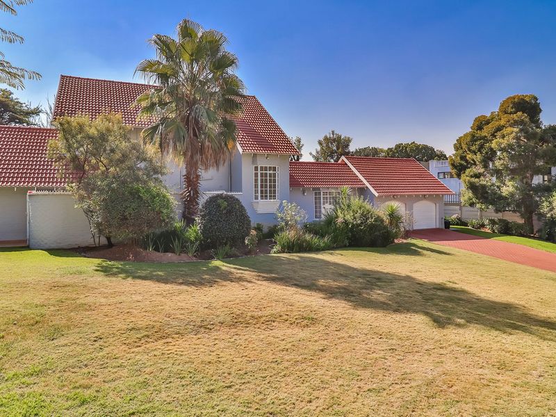 A well-maintained residential property featuring a classic terracotta tiled roof, a spacious front lawn, and a paved driveway leading to a double garage.