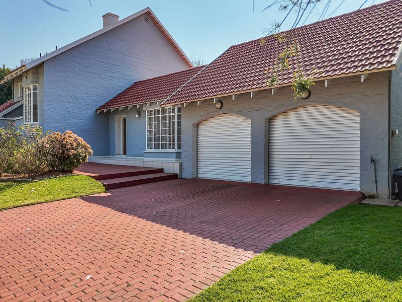 Front view of a residential property featuring a double garage, brick paved driveway, and well-maintained garden area.