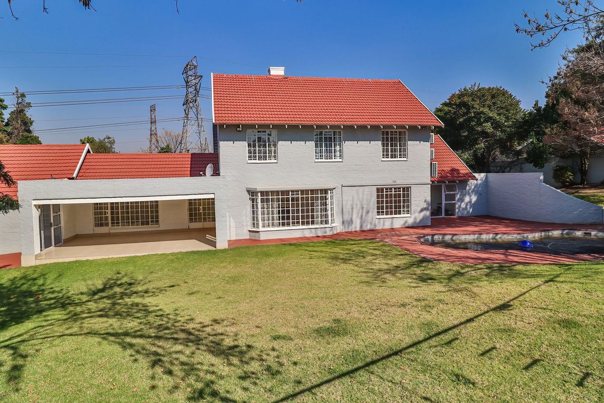 Rear view of a two-story house featuring a red tile roof, covered patio, swimming pool, and a spacious lawn area.