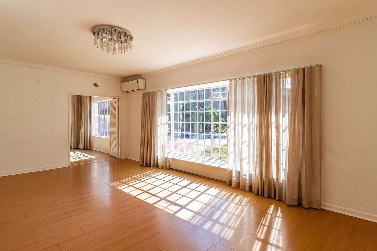 Spacious, light-filled living room featuring laminate flooring, crown molding, and a large window overlooking the garden, ready for personalization.