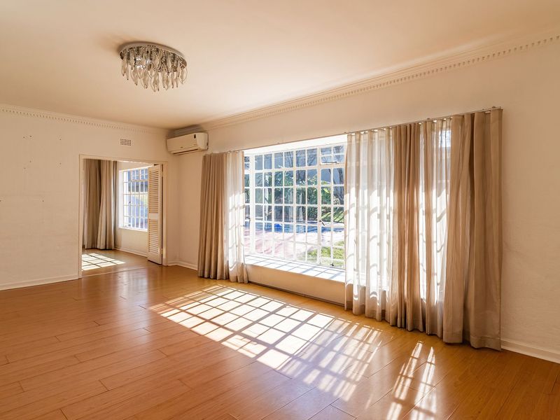 Spacious, light-filled living room featuring laminate flooring, crown molding, and a large window overlooking the garden, ready for personalization.