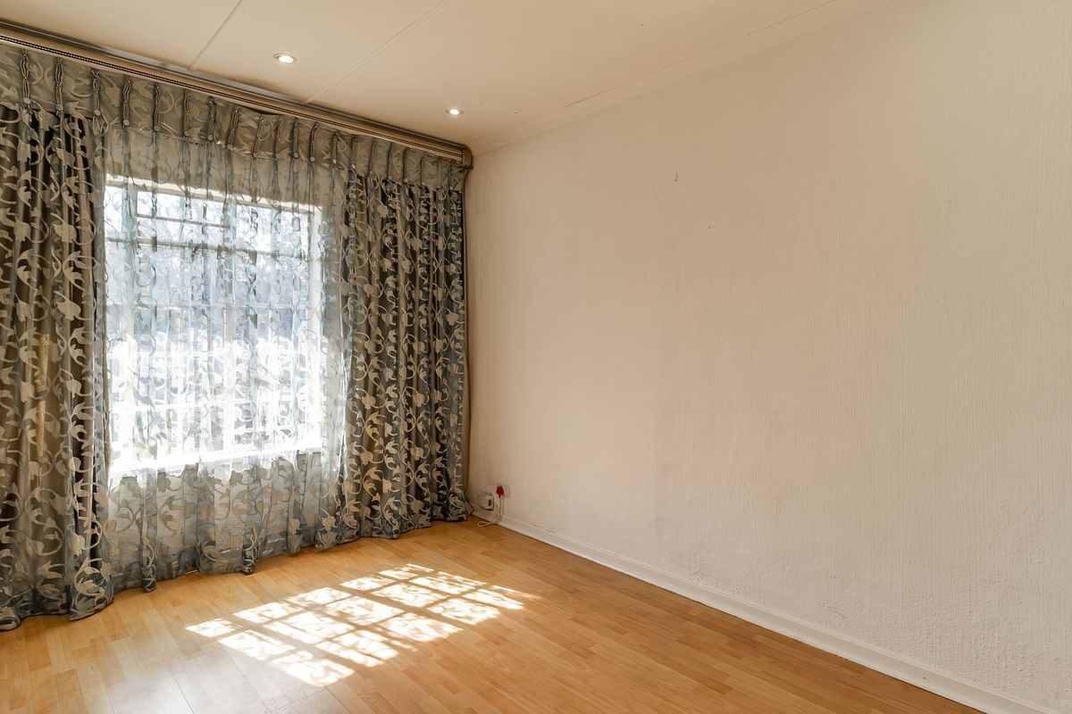 A bright, empty bedroom featuring laminate flooring, recessed downlighting, and large windows with installed curtain tracks.