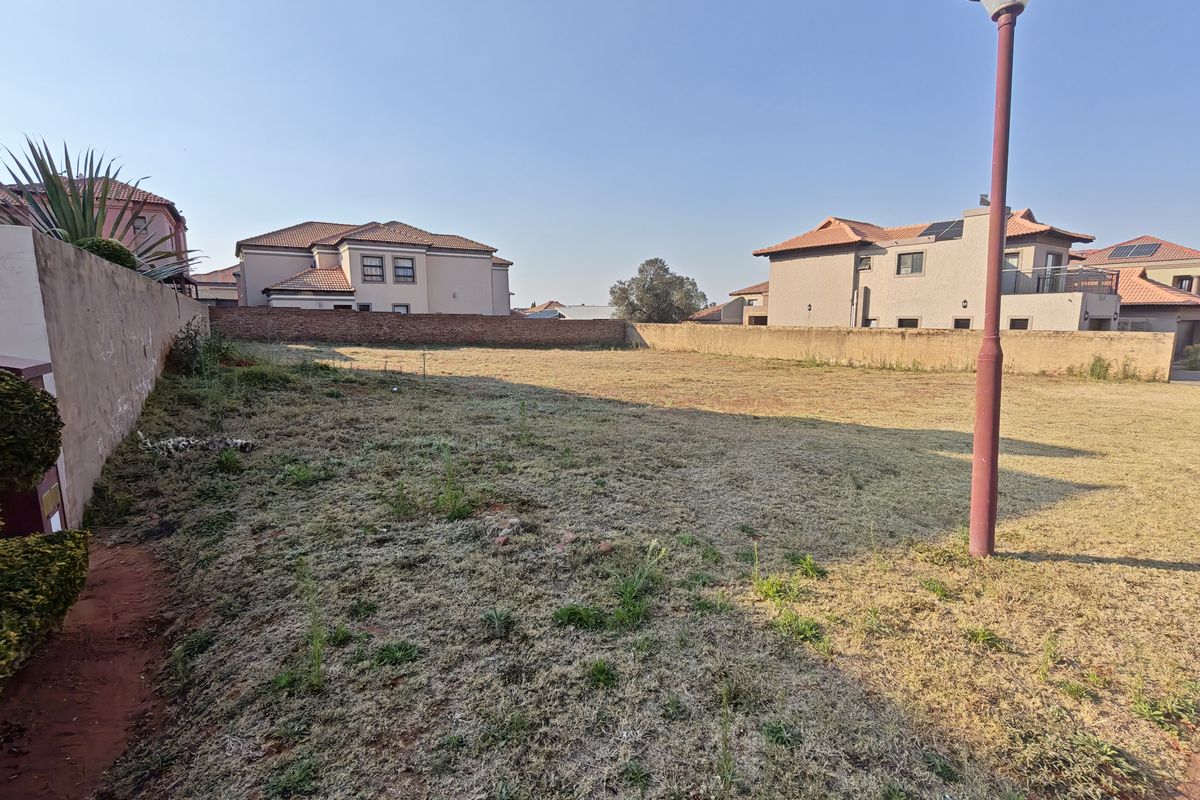 A vacant residential plot enclosed by perimeter brick walls, featuring a level grass surface and an existing street lamp.