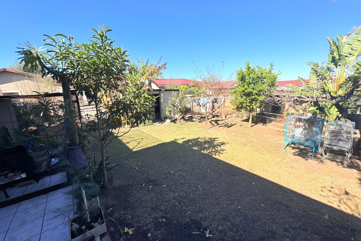 A spacious rear garden featuring a lawn area, tiled patio section, and perimeter fencing, offering potential for landscaping and outdoor living.