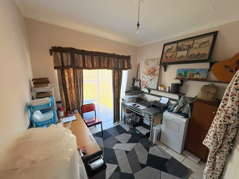 A functional bedroom space featuring tiled flooring and built-in shelving, currently utilized as a home office and storage area.