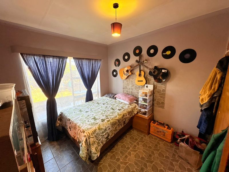 A bedroom featuring tiled flooring, a central pendant light fixture, and a large window providing natural light.